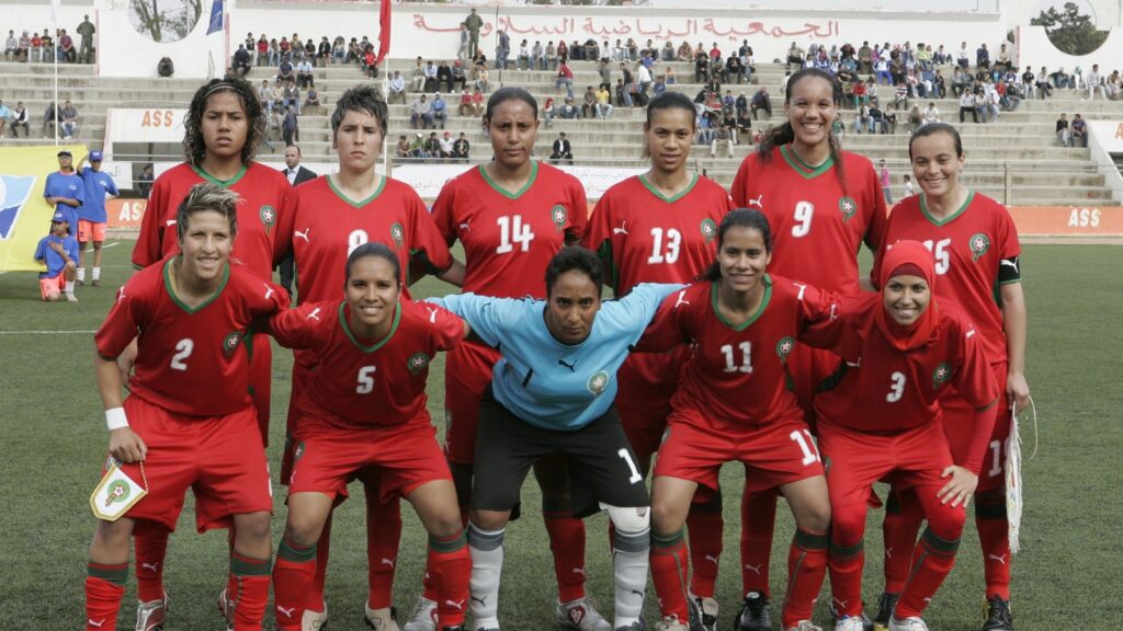 L’équipe nationale féminine du Maroc pose avant une rencontre, en maillot rouge, sur un terrain de football.